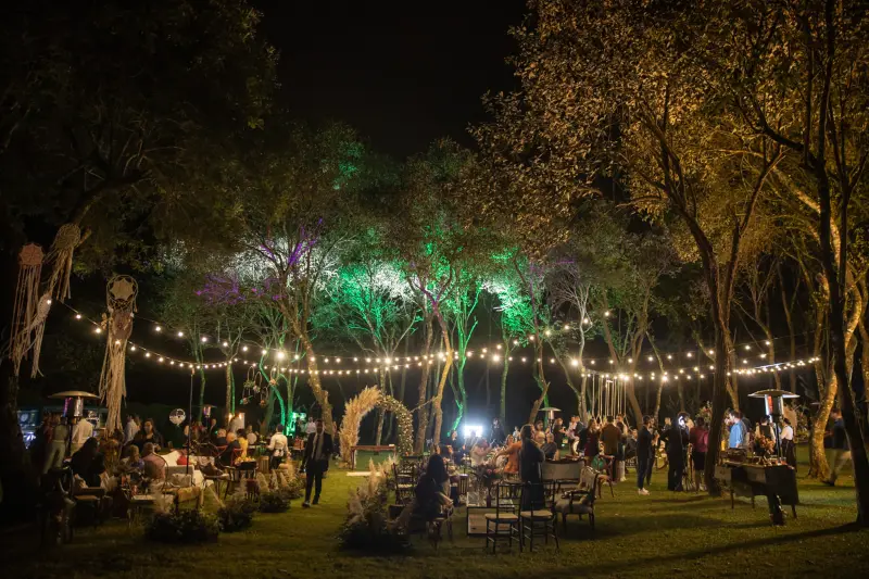 recep&ccedil;&atilde;o de casamento noturna ao ar livre, com ilumina&ccedil;&atilde;o por varais de luzes suspensos entre as &aacute;rvores,