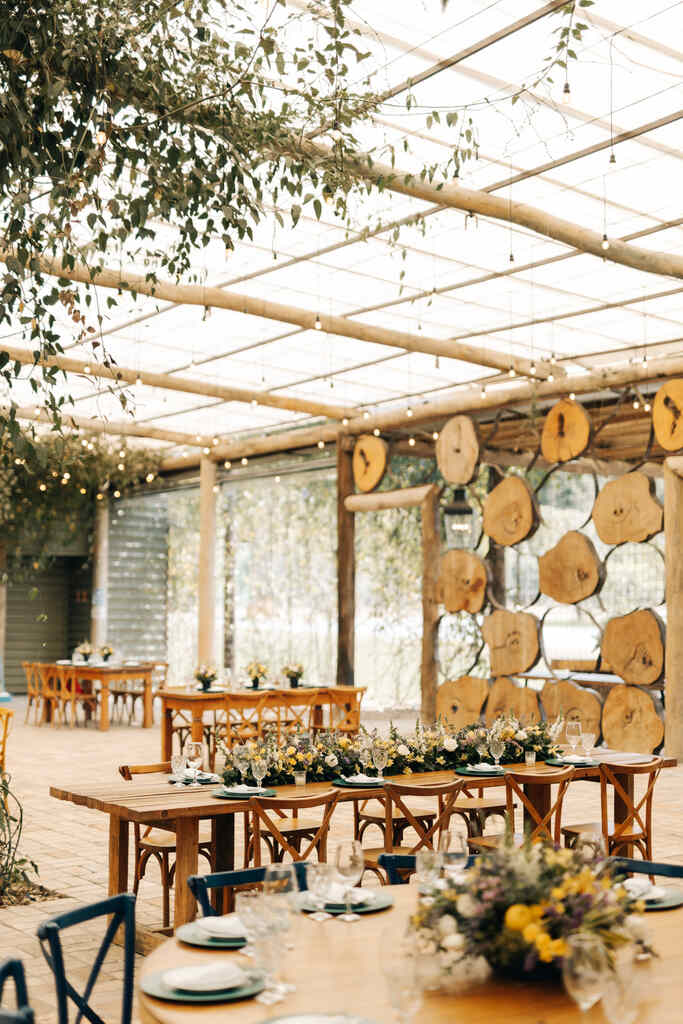 salão rústico com parede com troncos de madeira e mesa decorada com flores amarelas e brancas