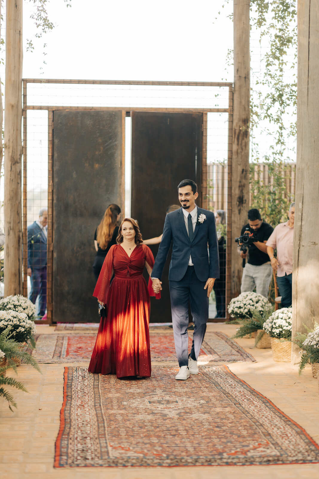 entrada do noivo com terno azul marinho de mãos dadas com mãe com vestido vermelho
