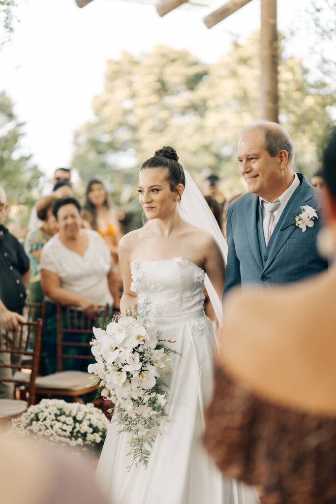 entrada da noiva com buquê de orquideas brancas ao lado do pai com terno azul