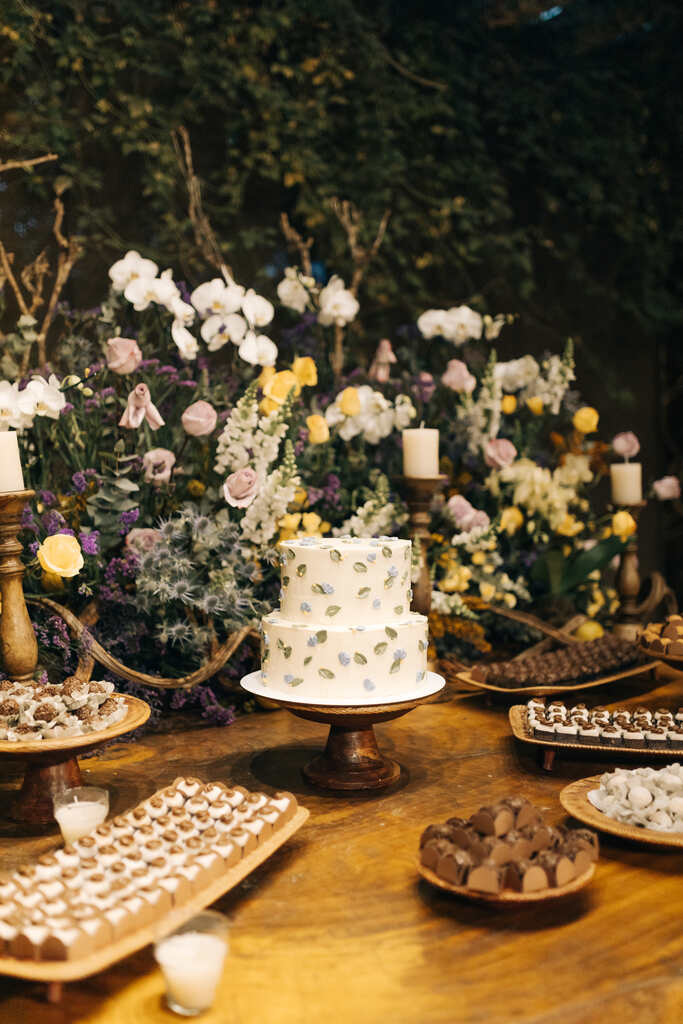 salão à noite com mesa rústica com bolo de casamento com detalhes azuis e flores brancas e amarelas