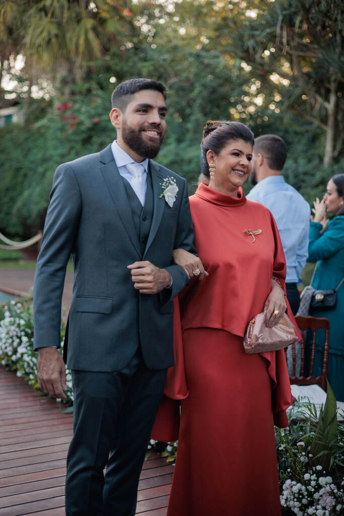entrada do noivo com terno cinza com colete ao lado da mãe com vestido vermelho