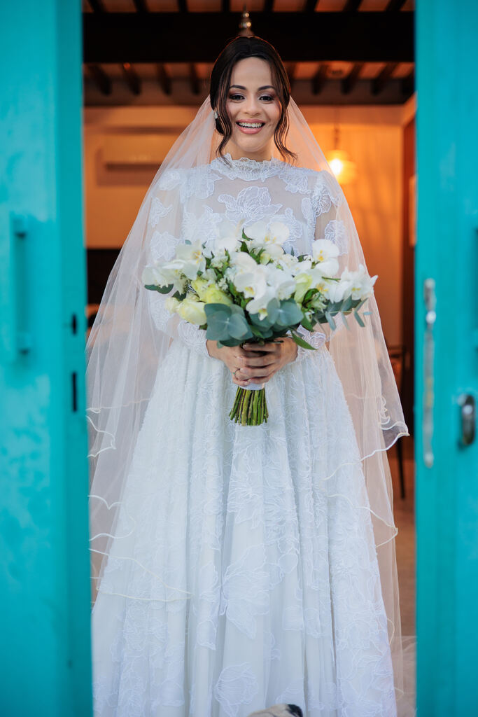 mulher com vestido de noiva com manga longa bordado com véu longo e buquê branco