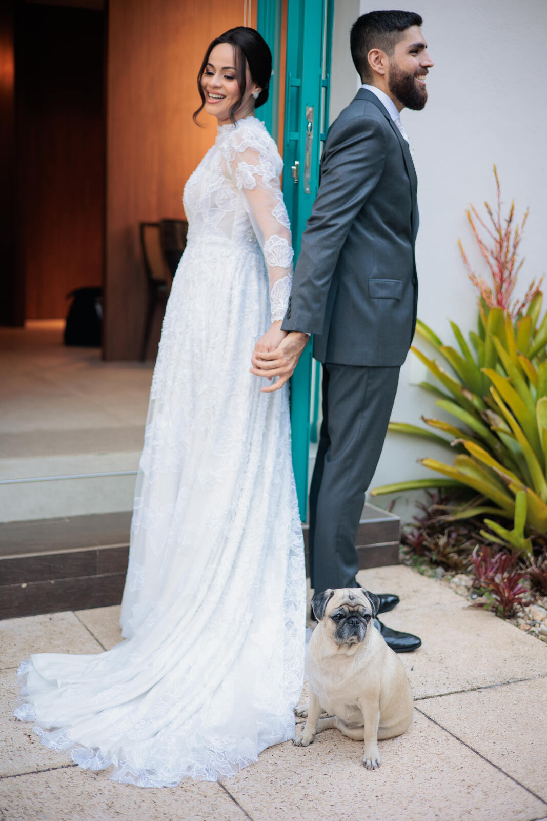 mulher com vestido de noiva com manga longa bordado e cabelo preso de costas de mãos dadas com noivo com terno cinza