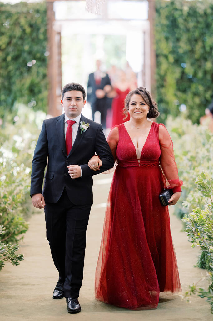entrada dos padrinhos com terno preto e gravta vermelha e mulher com vestido vermelho com decote em v