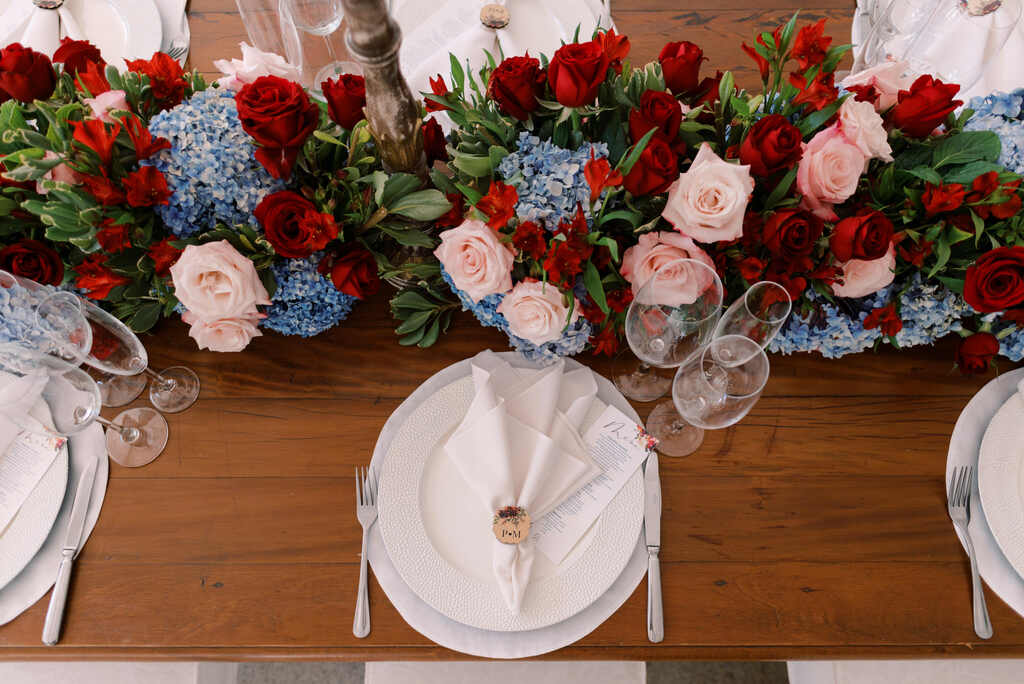 mesa posta decorada com rosas vermelhas e rose e hortensias azuis