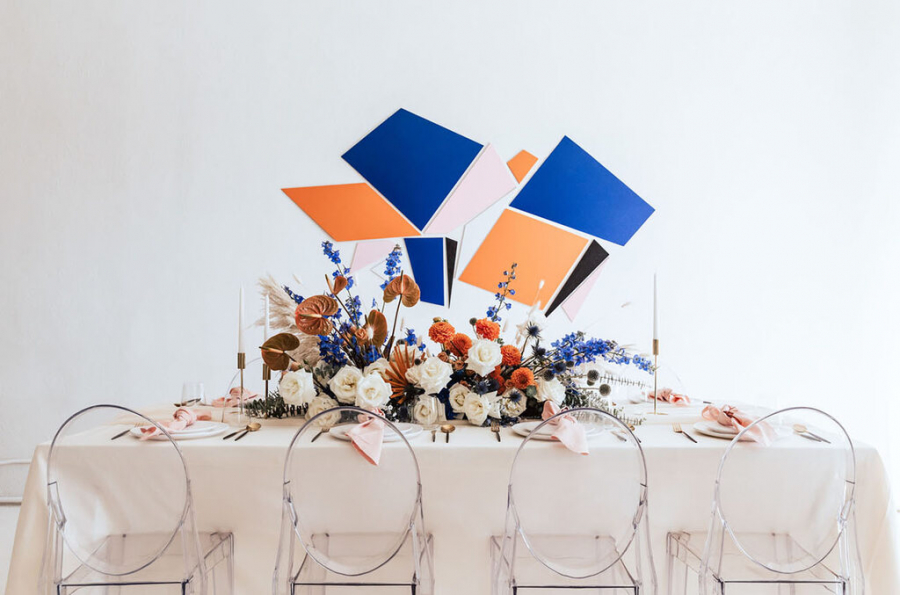 Mesa de festa de casamento, com elementos geométricos e coloridos, flores sobre a mesa e cadeiras de acrílico transparentes