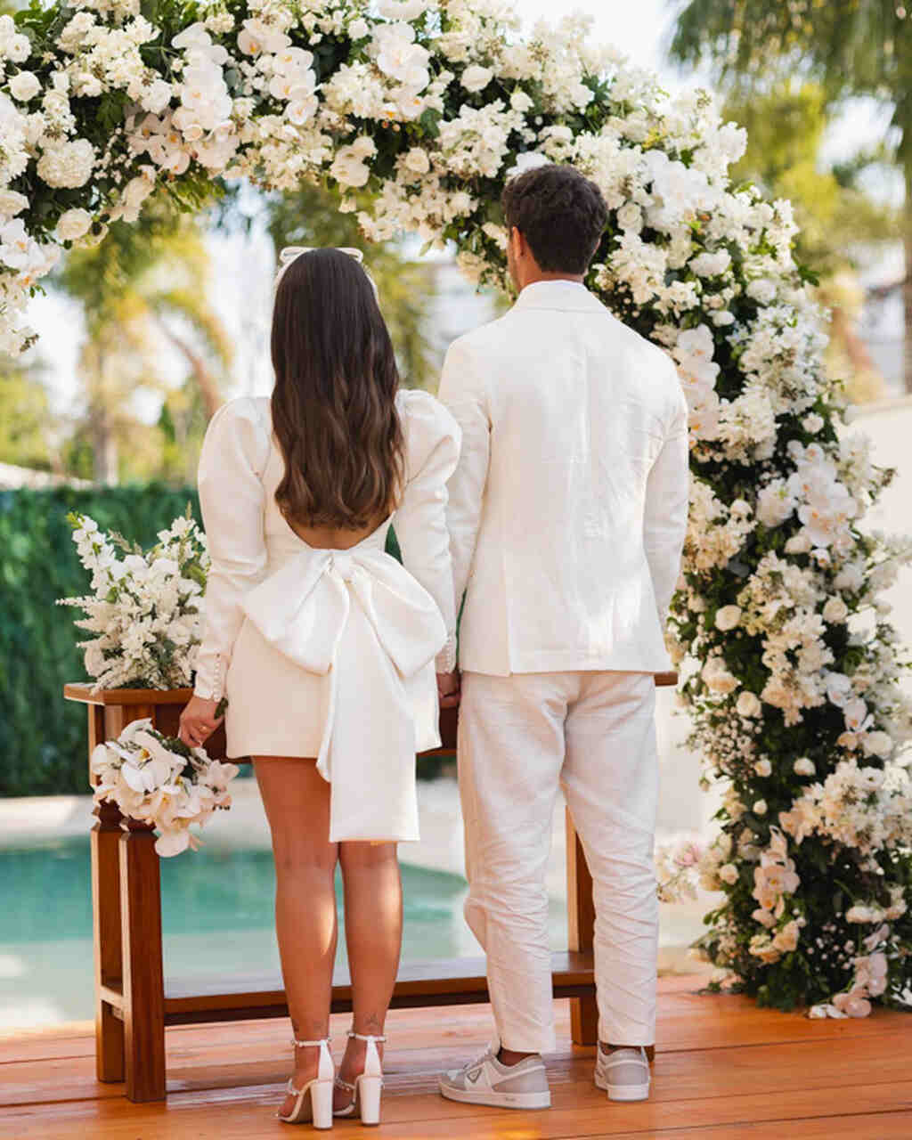 Noivos de frente para o altar, foto mostrando costas do casal com decoração de flores brancas
