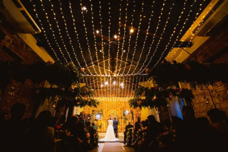 cen&aacute;rio de cerim&ocirc;nia de casamento com ilumina&ccedil;&atilde;o de teto feita por varais de luzes
