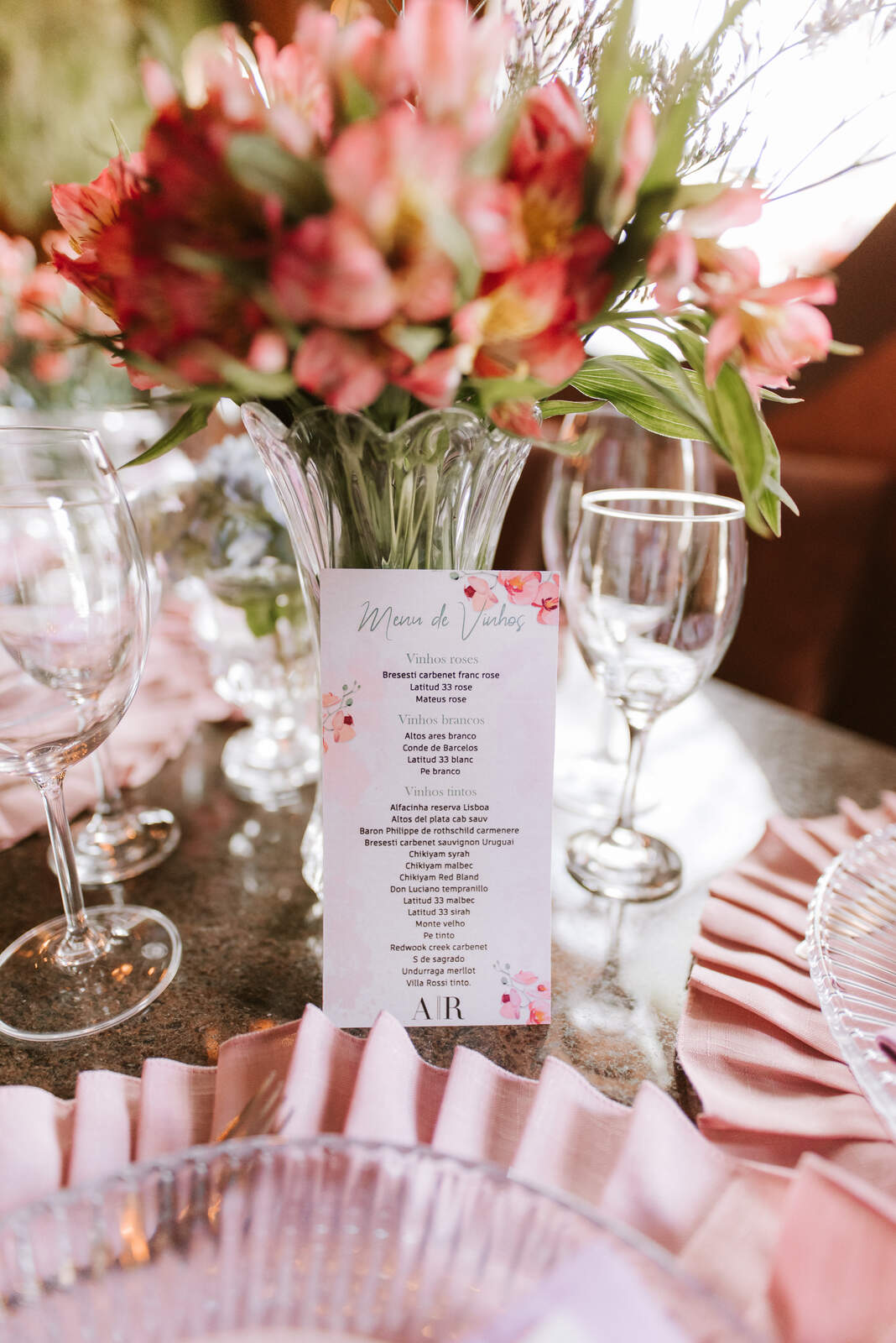 carta de vinhos no centro da mesa com vaso de flores cor de rosa e taças