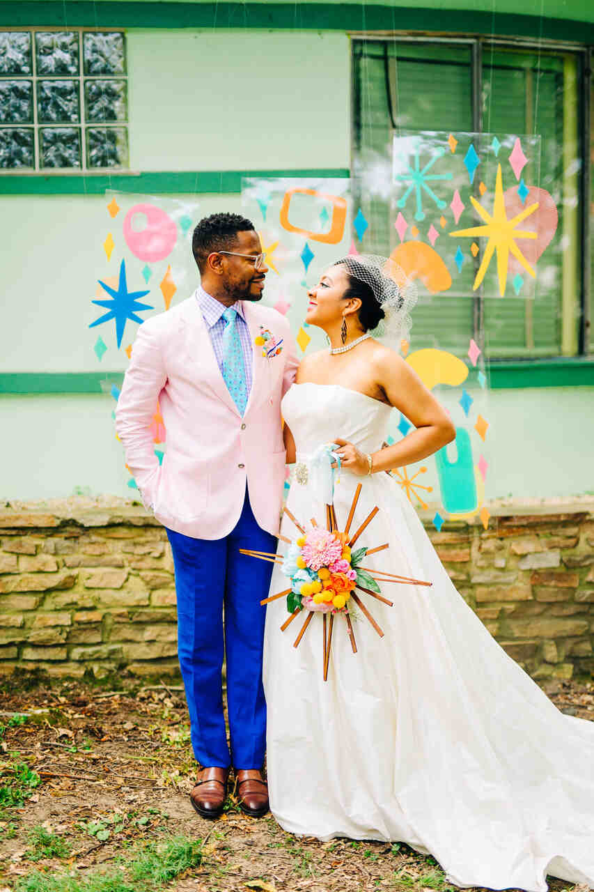 Casal de noivos com trajes de casamento diferentes, coloridos, com formas geométricas