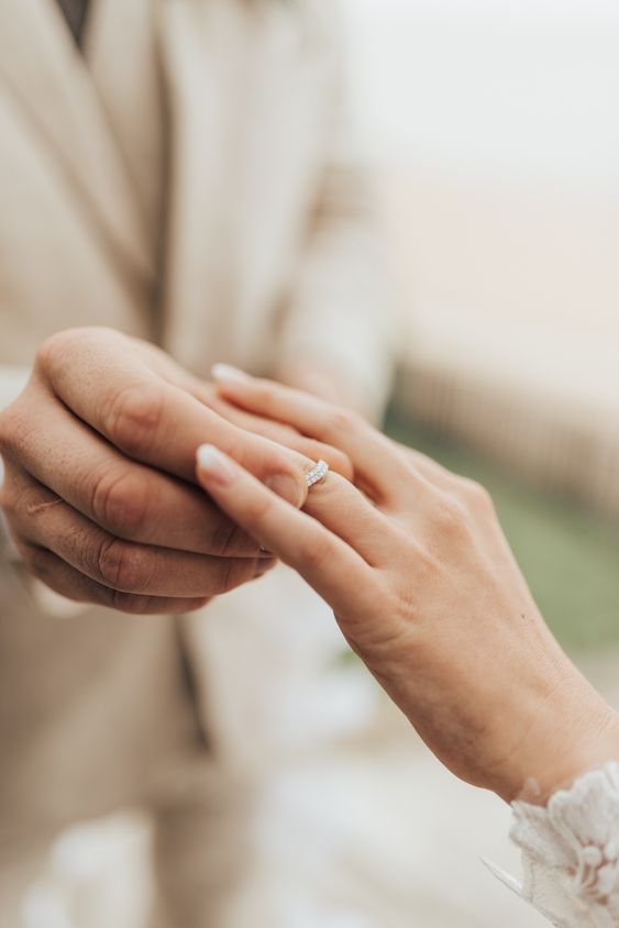 Noivo colocando aliança de casamento na mão da noiva.