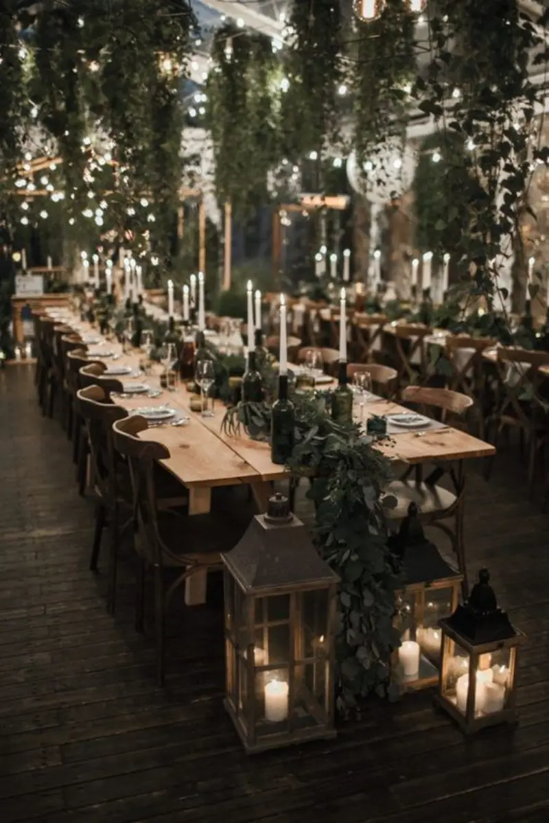 decora&ccedil;&atilde;o de recep&ccedil;&atilde;o de casamento em estilo r&uacute;stico chic e com mesas de madeira longa, ilumina&ccedil;&atilde;o intimista com velas e folhagens suspensas.