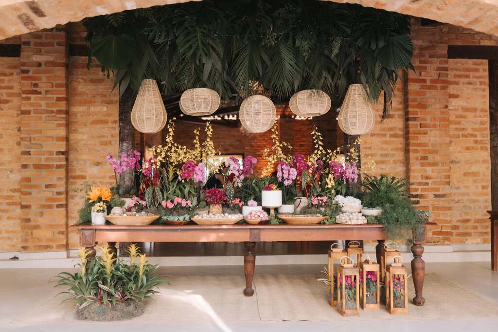 mesa de madeira com flores rosas amarelas laranjas e folhagens e luminarias naturais