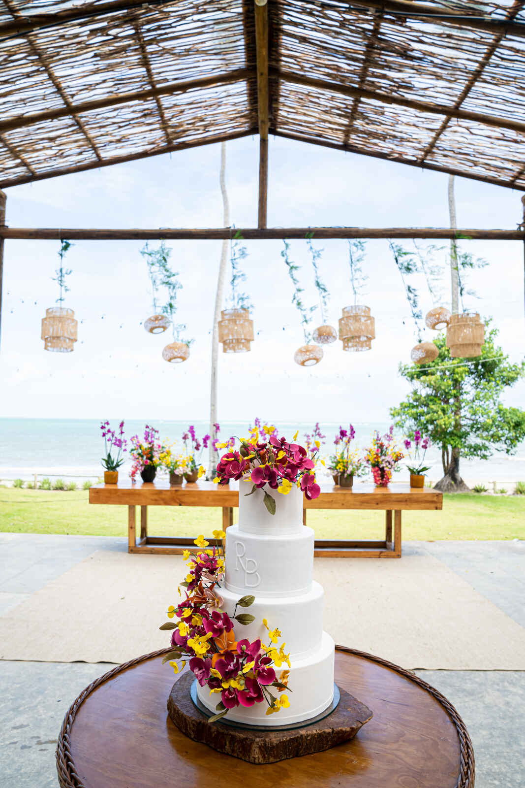 mesa de madeira com doces e orquideas e mesa redonda com bolo de casamento com 3 andares
