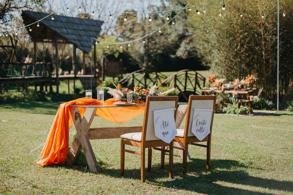mesa dos noivos com tecido laranja e cadeiras com bandeirolas