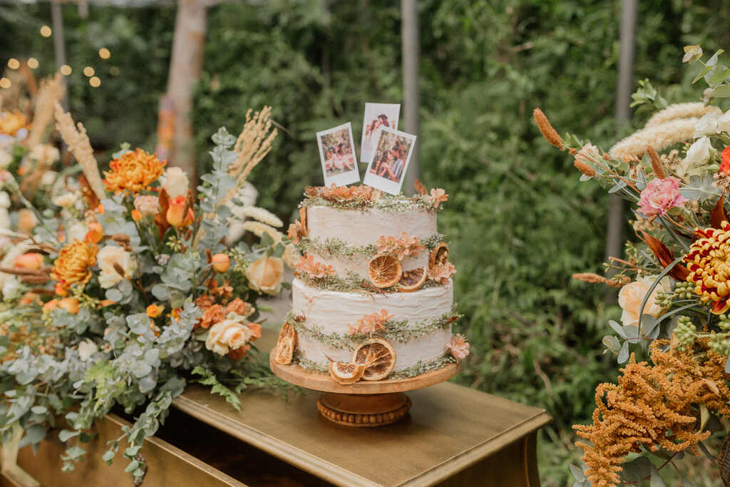 mesa do bolo com bolo de dois andares com laranjas secas e três fotos instantaneas em cima