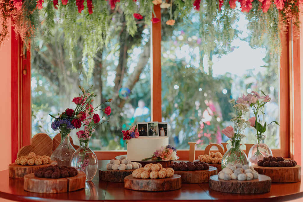 mesa de madeira redonda com flores coloridas doces de casamento e bolo de casamento branco com flores coloridas e topo com fotos polaroide