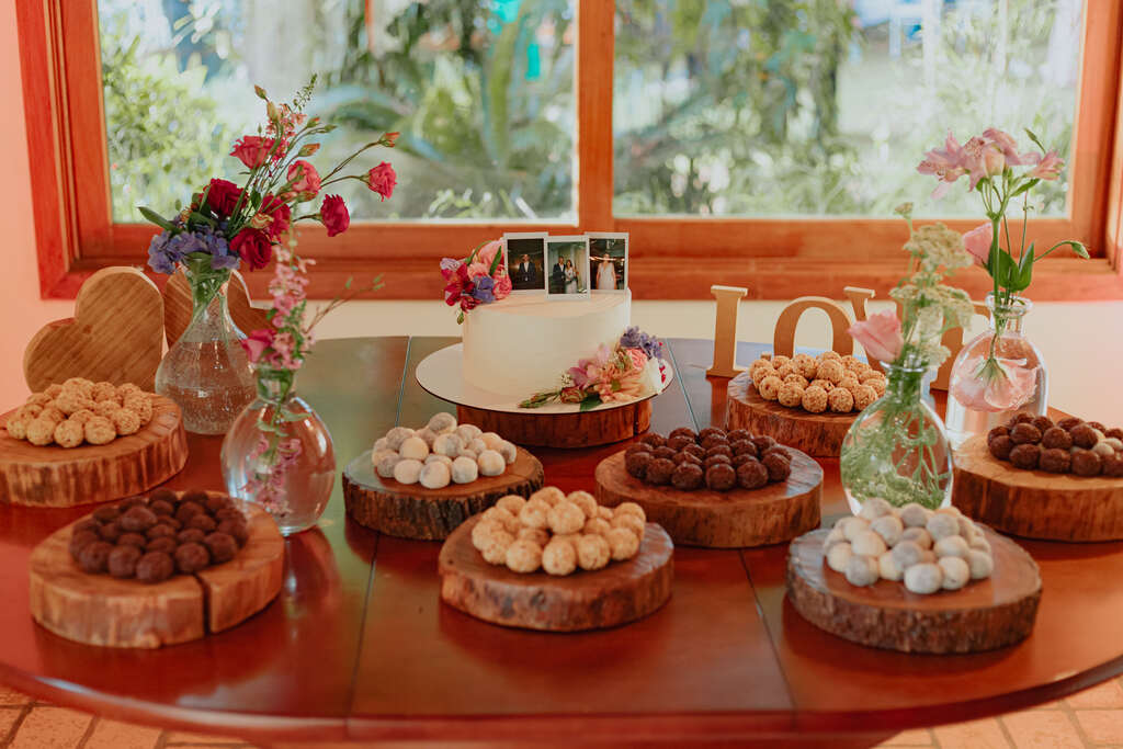 mesa de madeira redonda com doces de casamento e bolo de casamento branco com flores coloridas e topo com fotos polaroide
