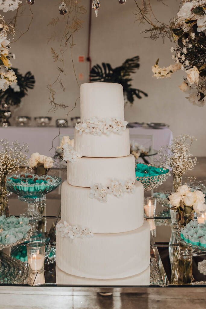 mesa prateada com bolo de casamento branco e flores brancas