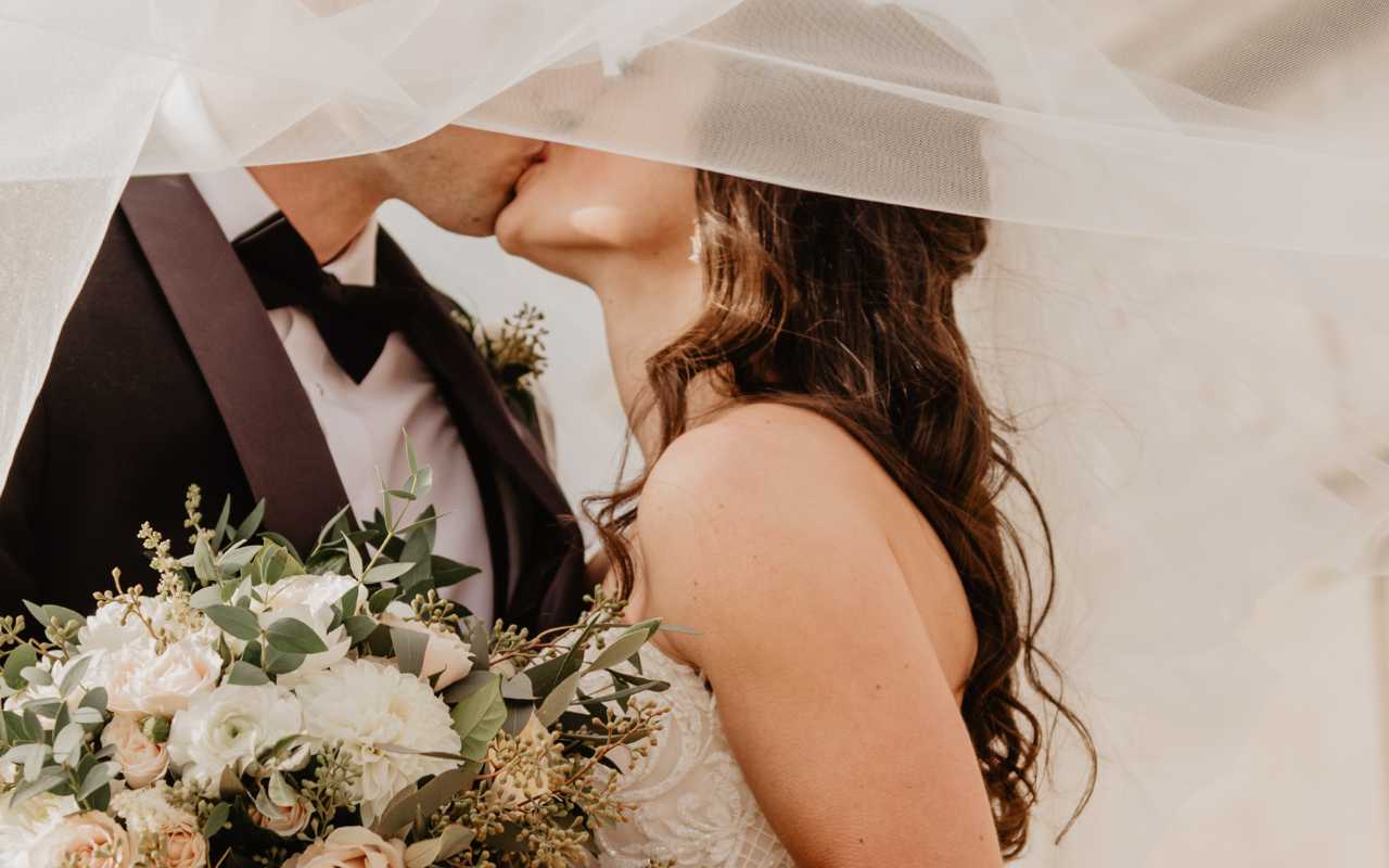 casal de noivos se beijando sob véu da noiva