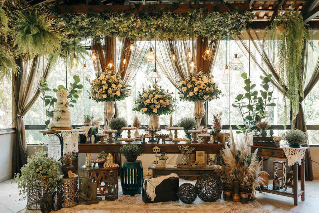 salão com mesa do bolo com três vasos com flores brancos