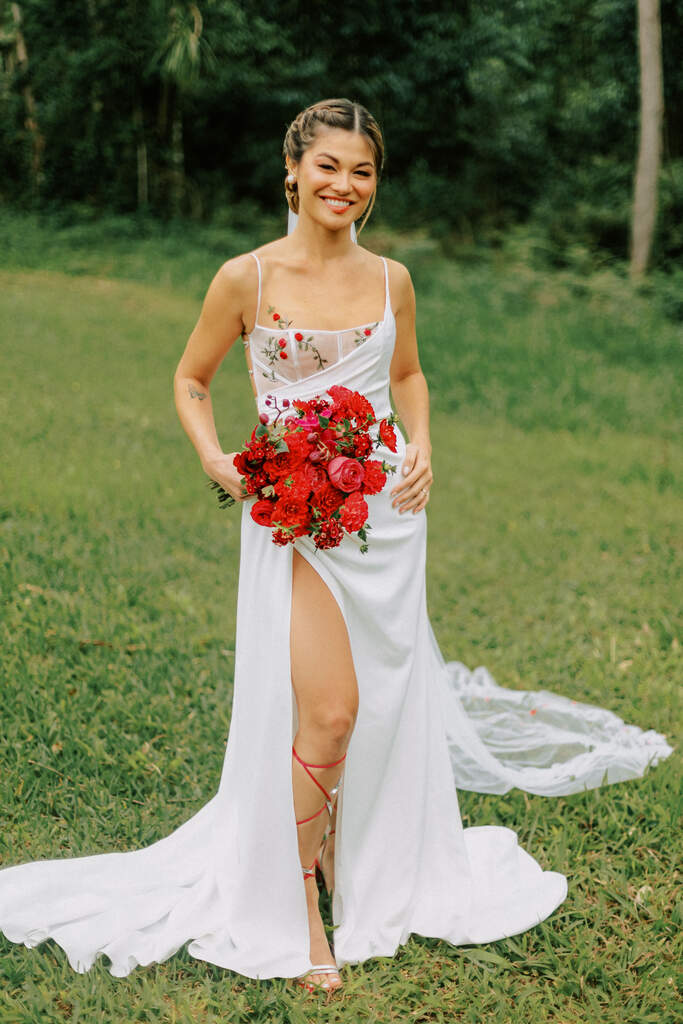 noiva com vestido com fenda segurando buquê com flores vermelhas