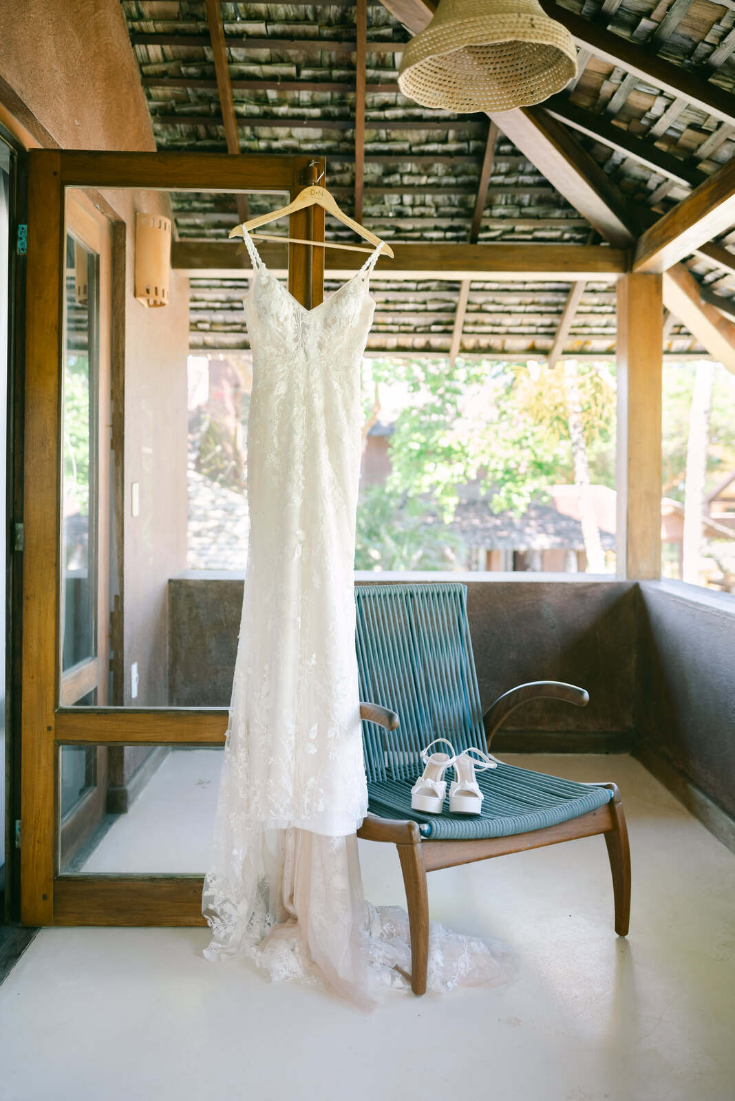 vestido de noiva de alças e renda ao lado de cadeira azul com sandálias de salto da noiva 