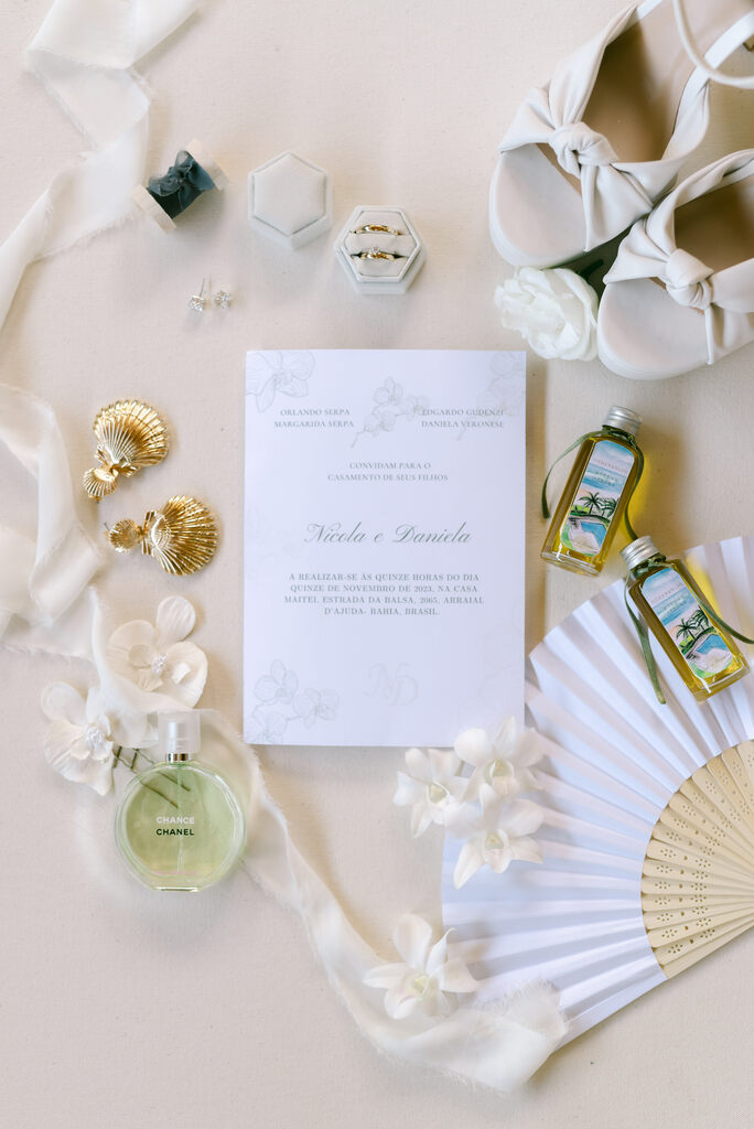 convite de casamento brnaco minimalista ao lado de leque tecido branco alianças e mini garrafinhas de azeite