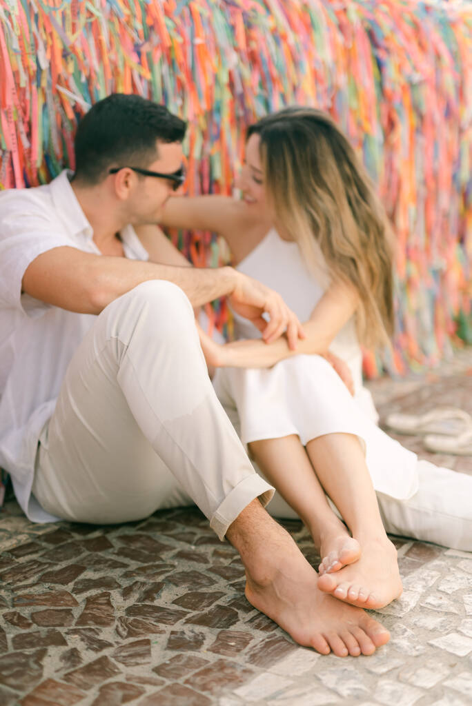 casal sentado perto de muro com fitinhas coloridas
