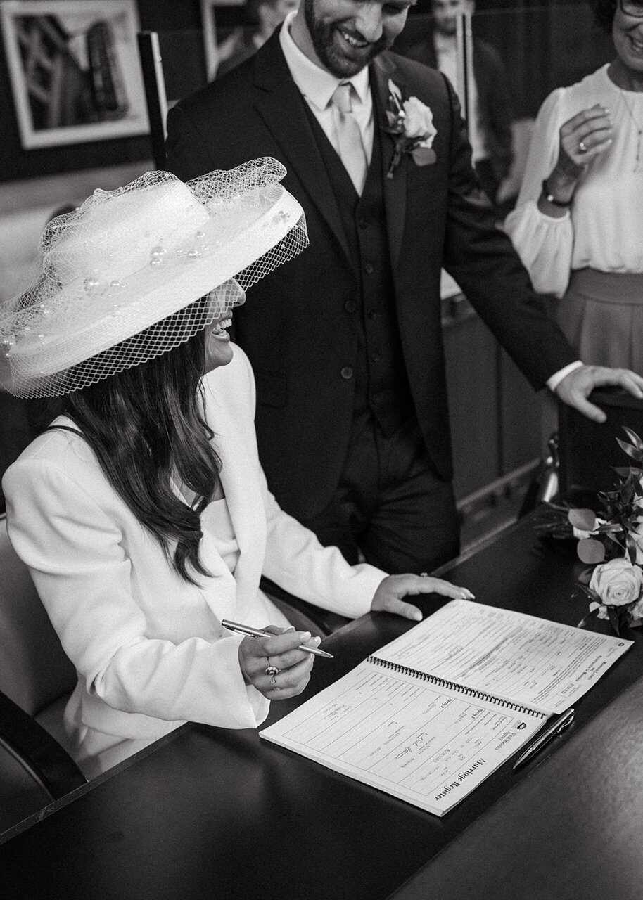 foto para casamento civil no cartório noiva com chapéu assinando certidão de casamento