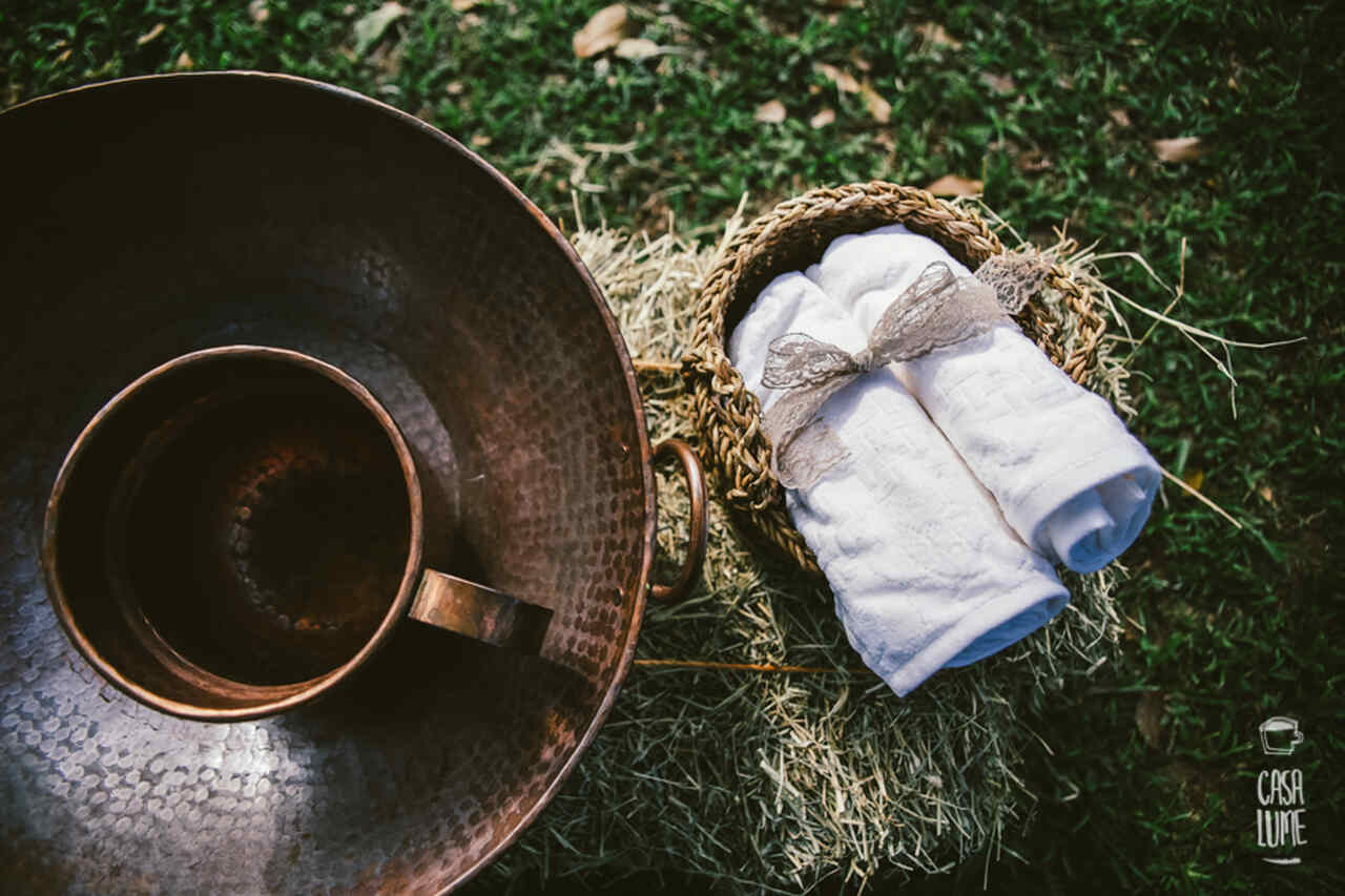 Itens de lava-pés - bacia e jarro de cobre e ao lado duas toalhas brancas enroladas