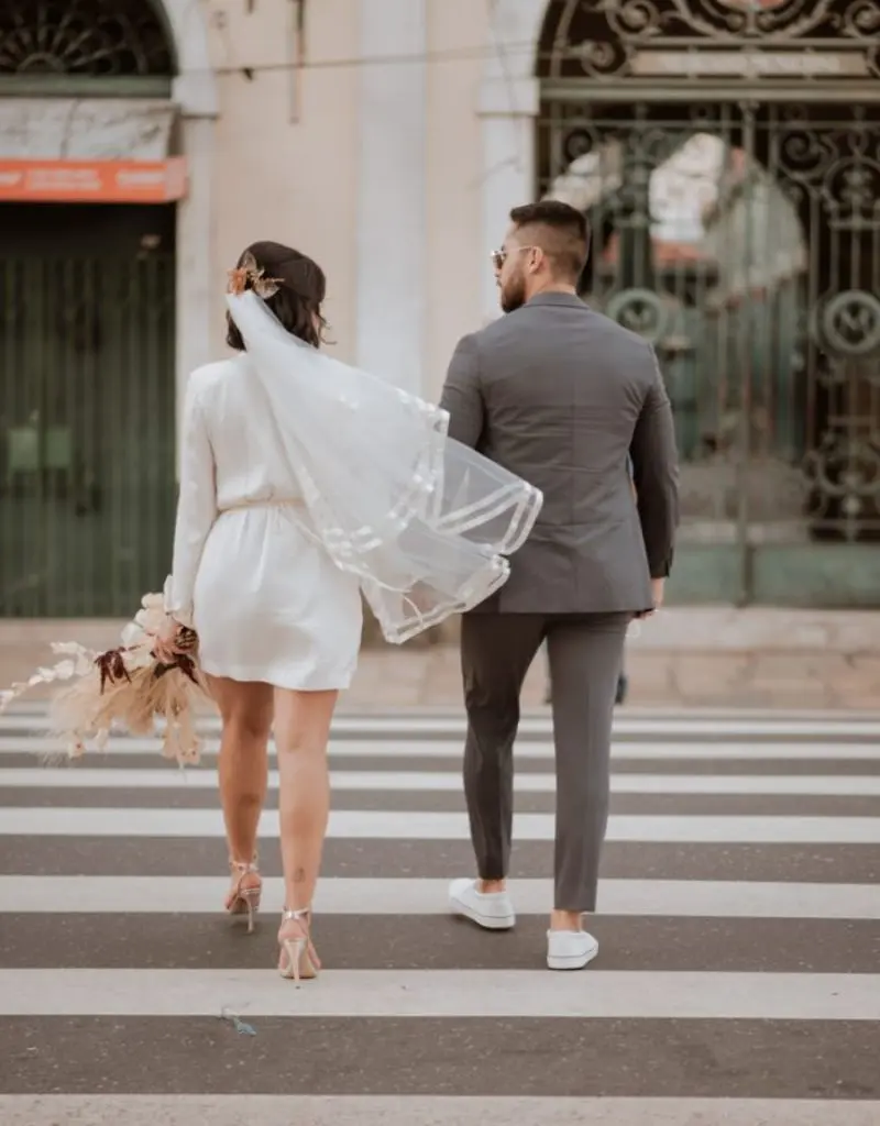 noivos caminhando na rua e ela está usando um vestido e véu curto