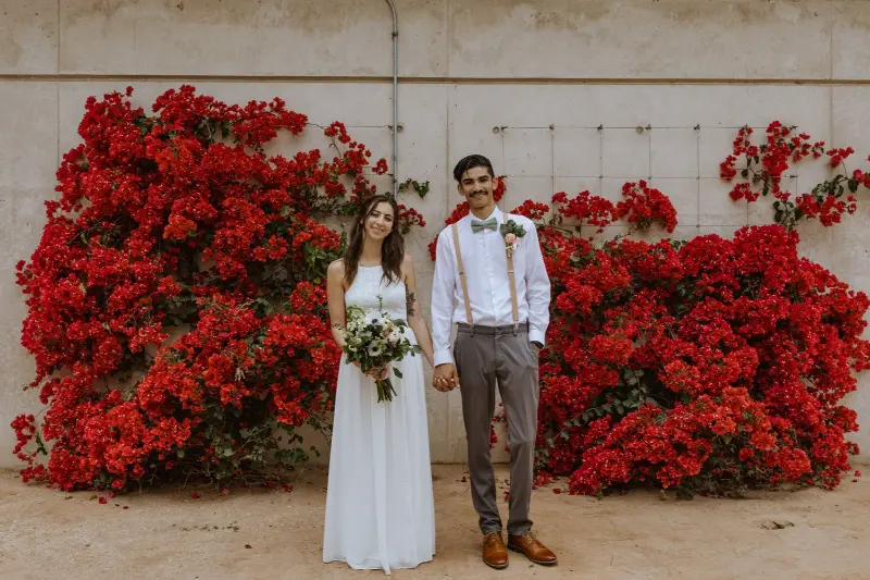 noiva veste um vestido branco longo e simples, enquanto o noivo usa calças cinzas, uma camisa branca, suspensórios e uma gravata borboleta.
