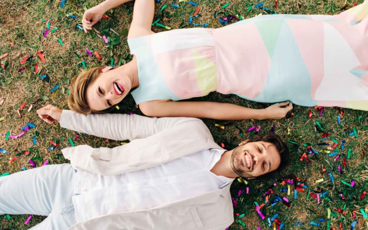 casal de noivos em casamento criativo deitado na grama com confete colorido