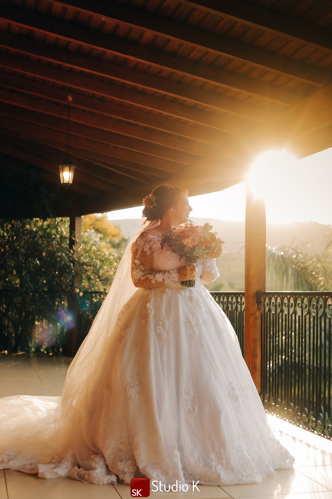 noiva com vestido clássico com manga longa bordada carregando buquê com flores rosas e vermelhas na varanda
