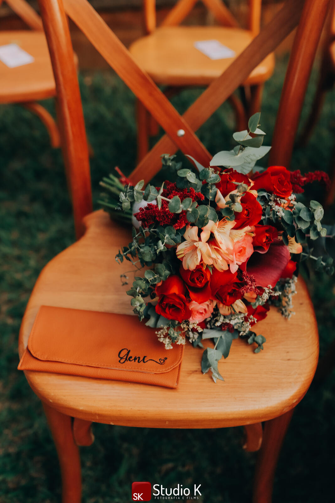 buquê com flores rosas e vermelhas em cima da cedira de madeira e ao lado de carteira marrom bordada