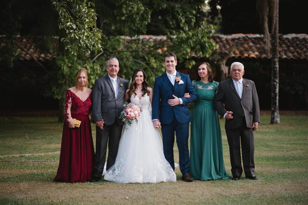 noivos ao lado dos pais com ternos cinza e mãe com vestidovermelho e verde
