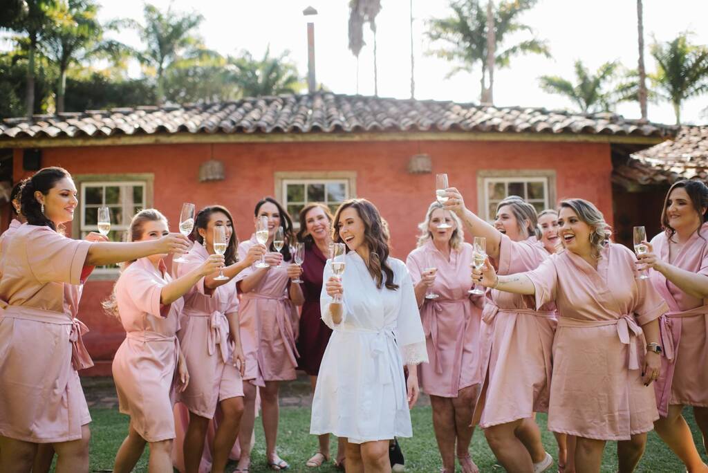 noiva com robe branco brindando com madrinhas com robe rosa no campo