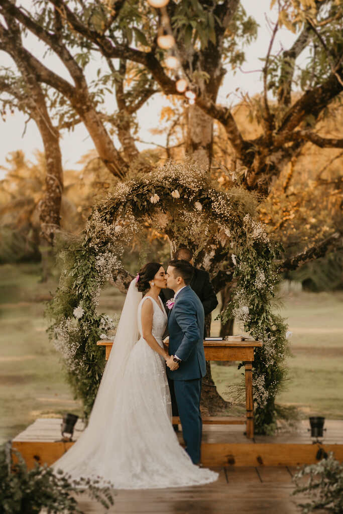 Noivos se beijando em frente ao altar, com um arco de flores ao fundo
