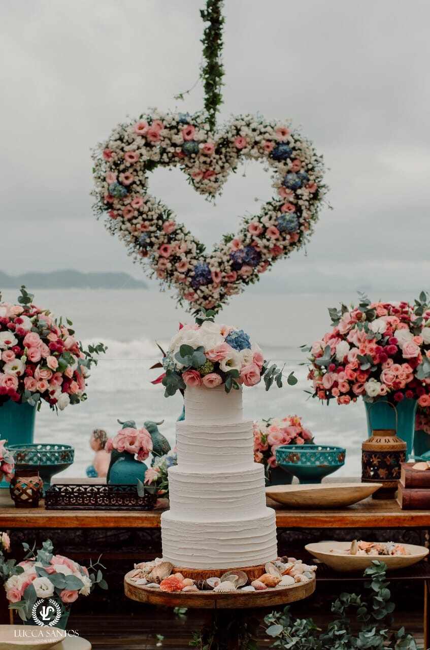 Mesa do bolo com uma guirlanda de flores em formato de coração. Arranjos florais em tons pastéis.