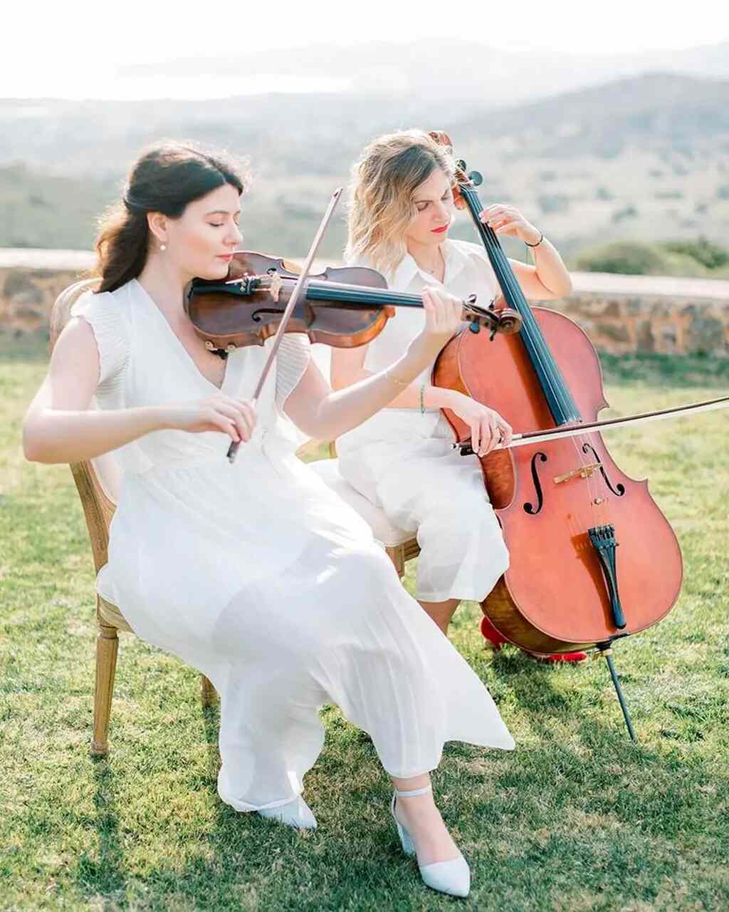 Duas mulheres sentadas ao ar livro tocando instrumentos de corda