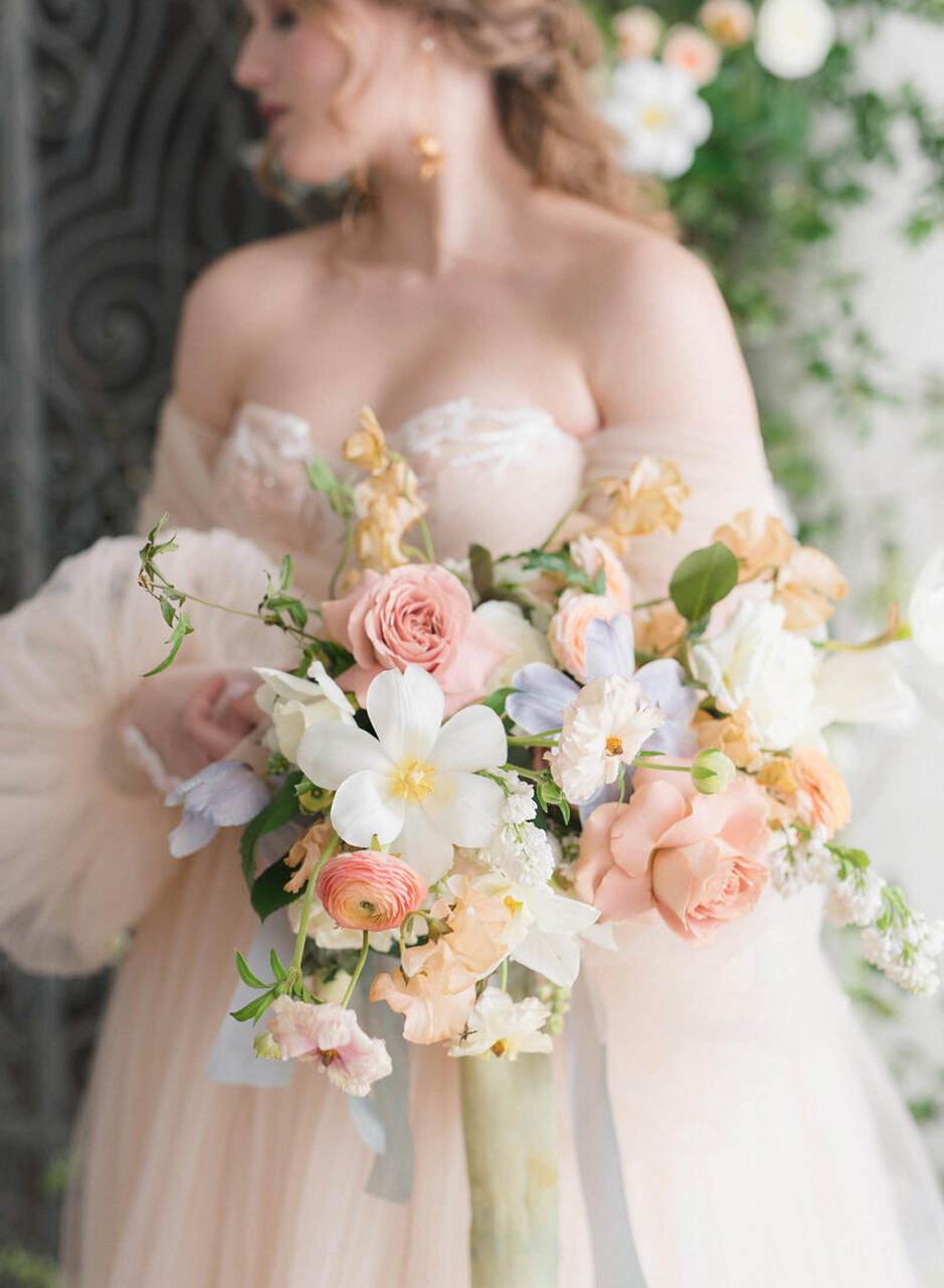 Buquê de flores em destaque em cores pastéis nas mãos de uma noiva.