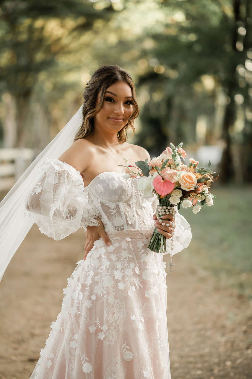 Noiva posando para a foto, com uma mão na cintura e a outra segurando um buquê de flores