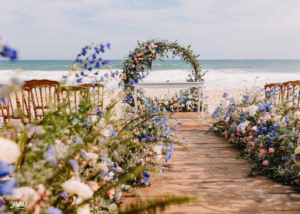 Cerimônia de casamento montada na praia, com um arco de flores no altar, uma passarela de madeira com flores