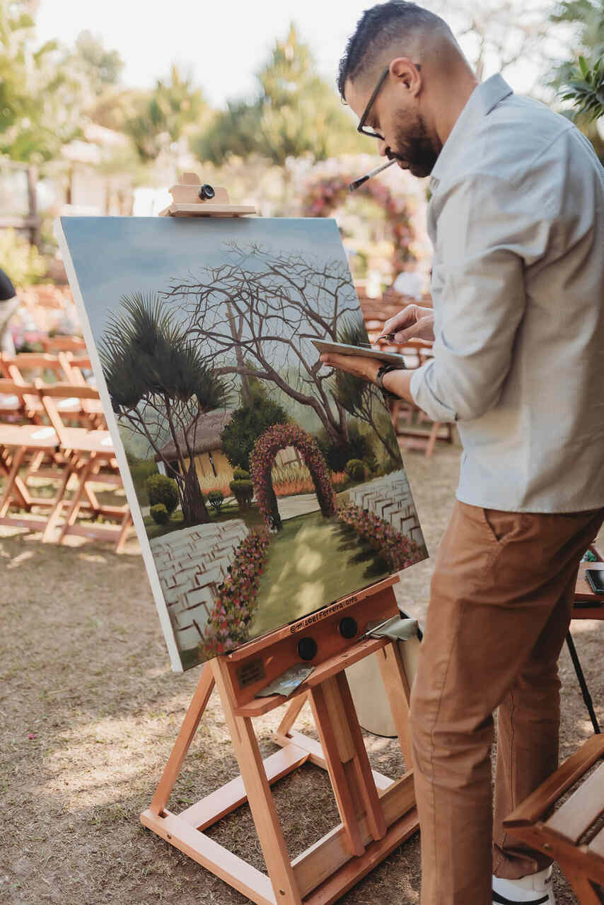  Quadro com pintura do cenário do casamento. Um homem está pintando o quadro.