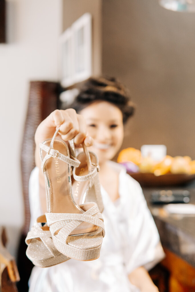 noiva com robe branco segurando sandália meia pata na cor champagne