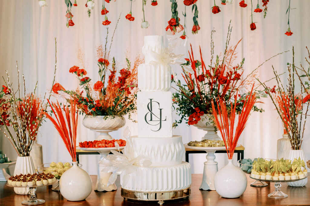 mesa com bolo de casamento branco com flores vermelhas pendentes