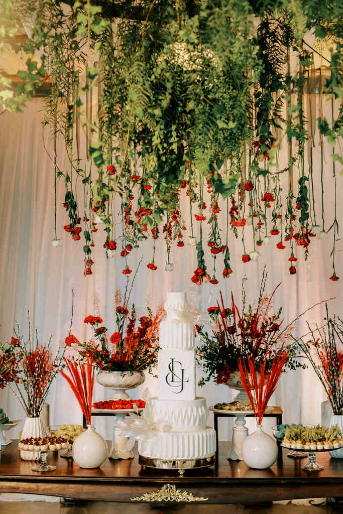 mesa com bolo de casamento branco com flores vermelhas pendentes