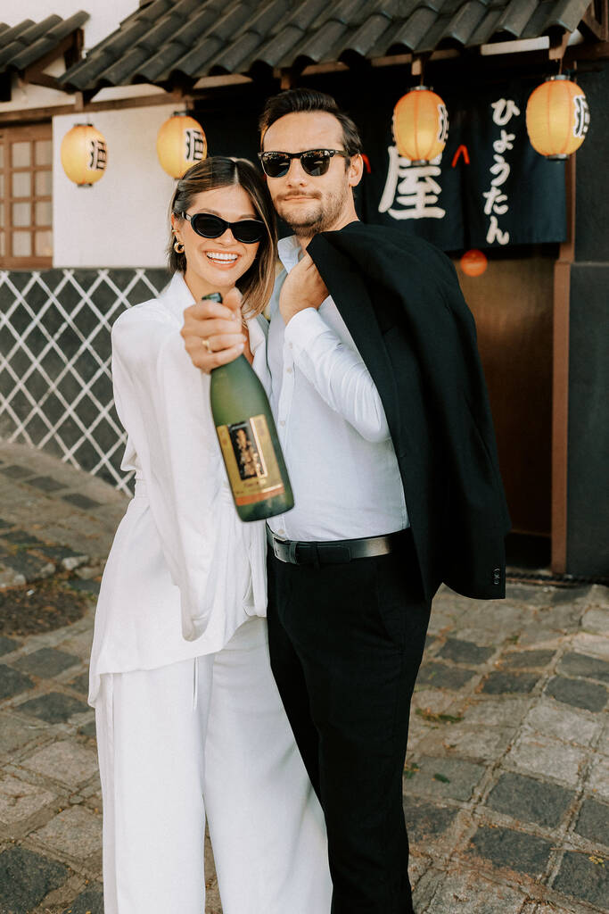 noivos na frente de bar japonês segurando garrafa de saquê
